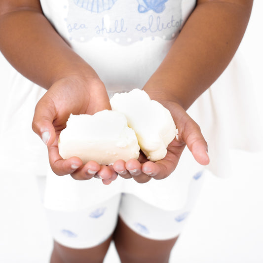 Child with white and blue two piece outfit holding two Cuddle Cleanse Cloud shaped soap