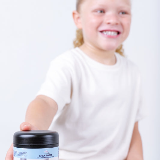 A blonde curly haired toddler holding a jar of Shea Sweet product against a white background