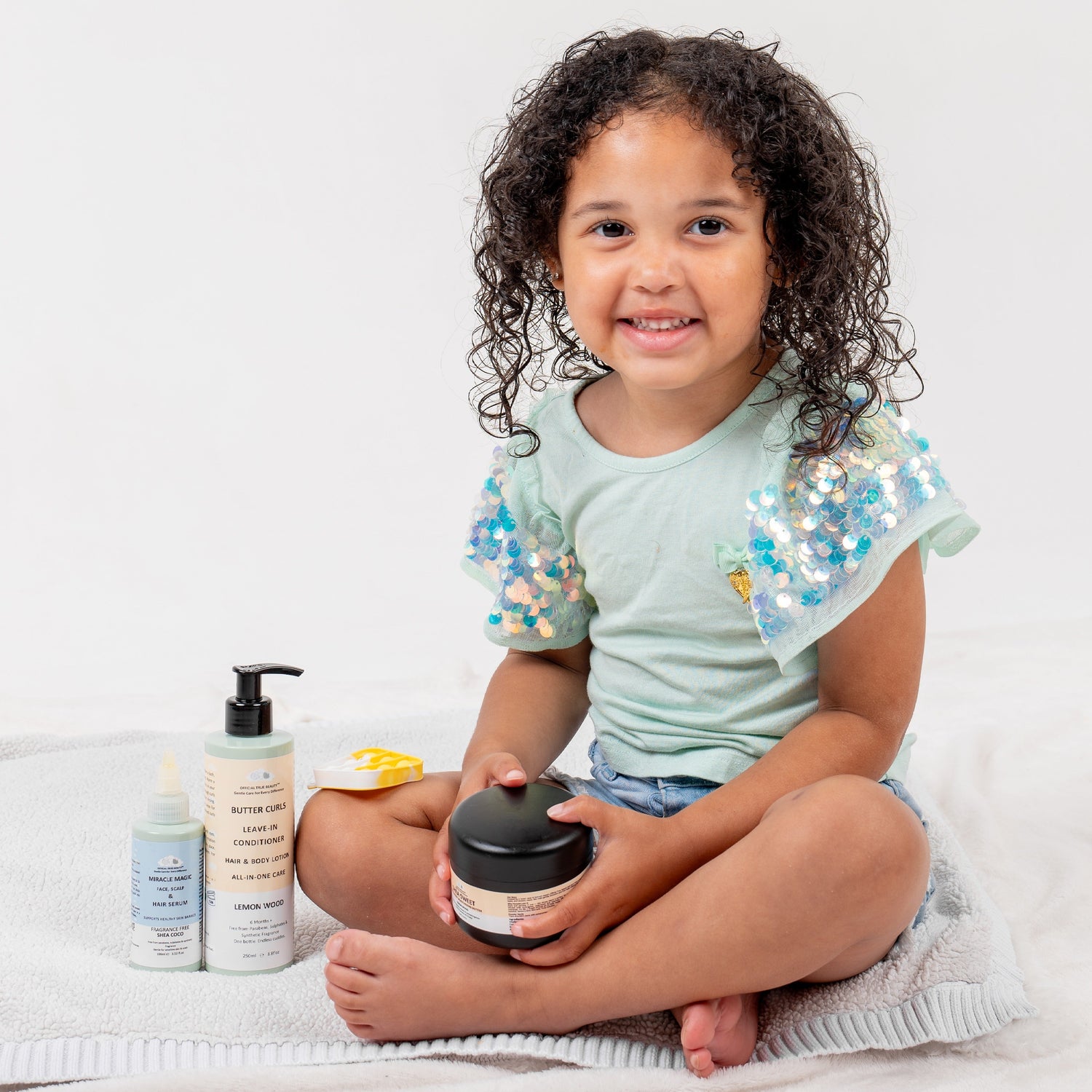 Smiling child with multiple products sat on a white blanket