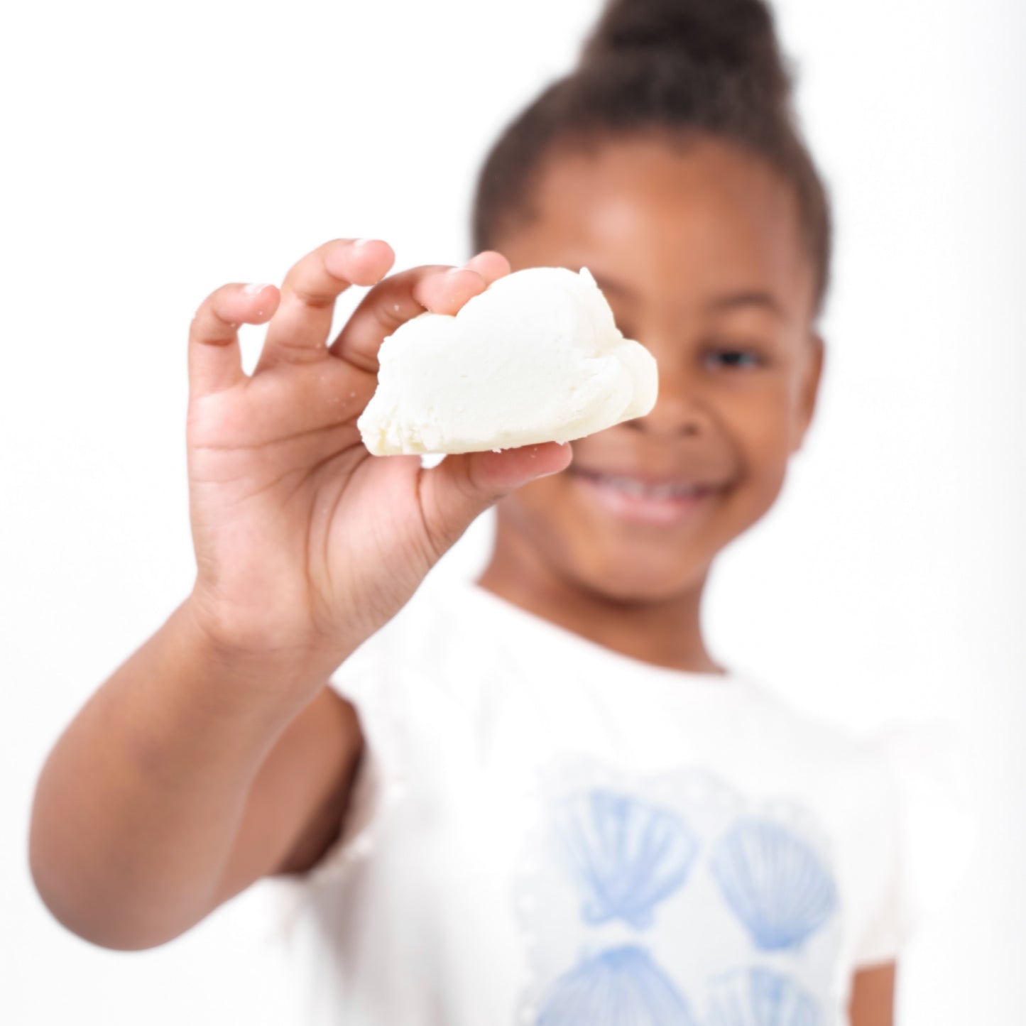 A Young girl holding a cloud-shaped Official True Beauty Cuddle Cleanse Soap in front of the camera