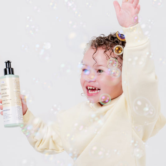 Curly hair Toddler holding Lemon Wood Butter Curls displayed in her right hand with bubbles around