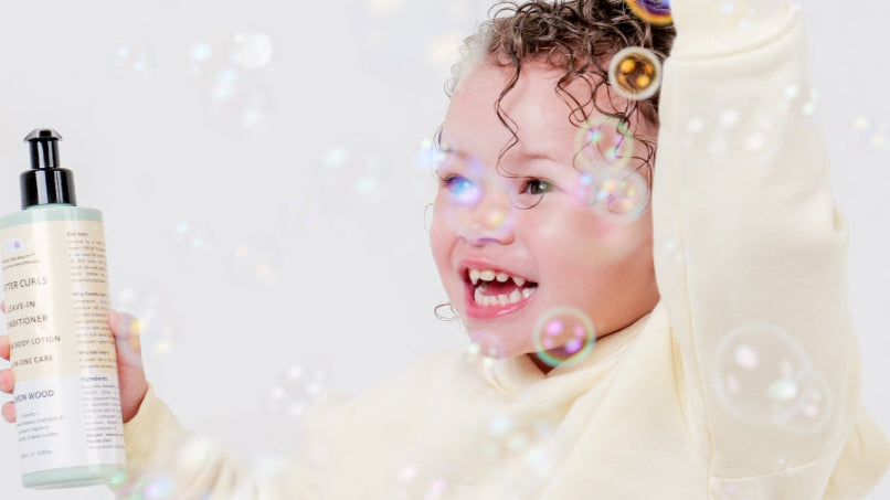 smiling child wearing yellow jumper  holding a bottle of lemon wood butter curls with bubbles around,