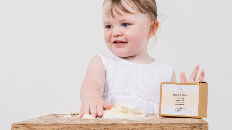 smiling girl moulding cuddle cleanse soap on a wooden surface
